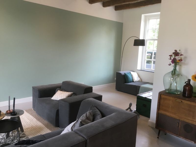 Industriële betonnen vloer in een woonkamer in Son, met grijze bank, salie­groene wand, houten balken en een vintage dressoir