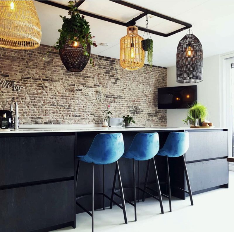 Keuken met een lichte Venetiaans woonbeton vloer in de kleur Grigio Cemento, zwart keukeneiland, bakstenen muur en rieten hanglampen