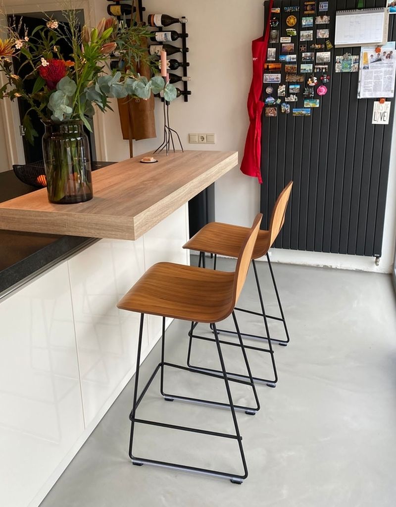 Quartz Stone gietvloer keuken met bar Lichtgrijze Quartz Stone gietvloer in een keuken met houten bar, twee houten barkrukken en een antraciet radiator