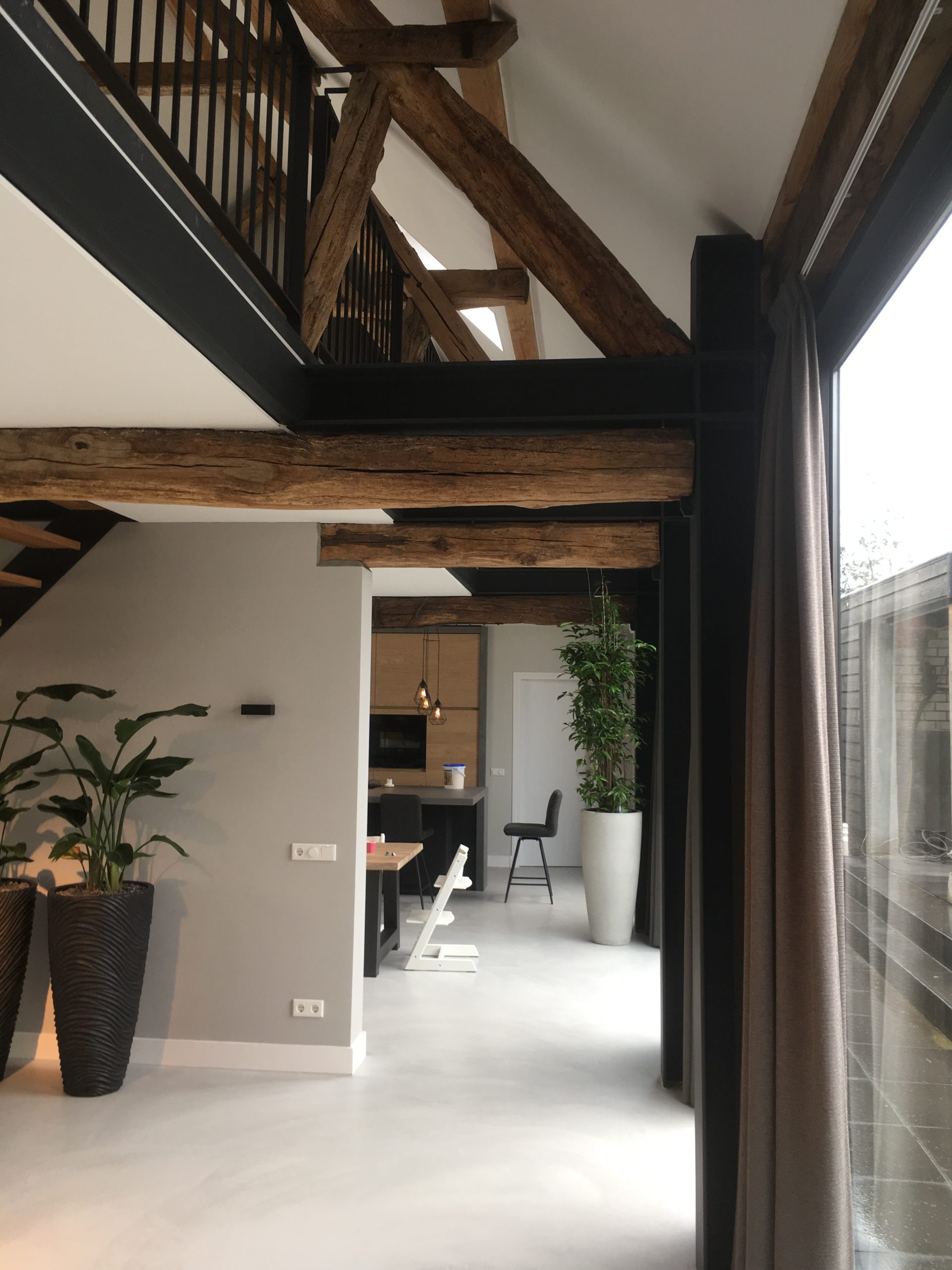 Beton ciré vloer in een gerenoveerde boerderij Moderne boerderij met zwarte stalen pui en oude houten balken, op een lichte beton ciré vloer
