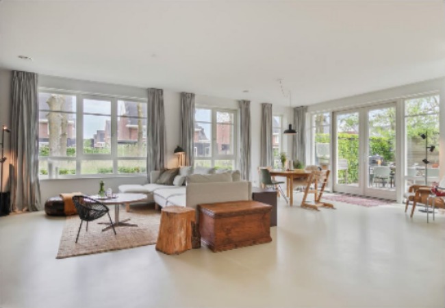 Lichte woonkamer met grote raampartijen en een naadloze microcement vloer in een warme zandtint