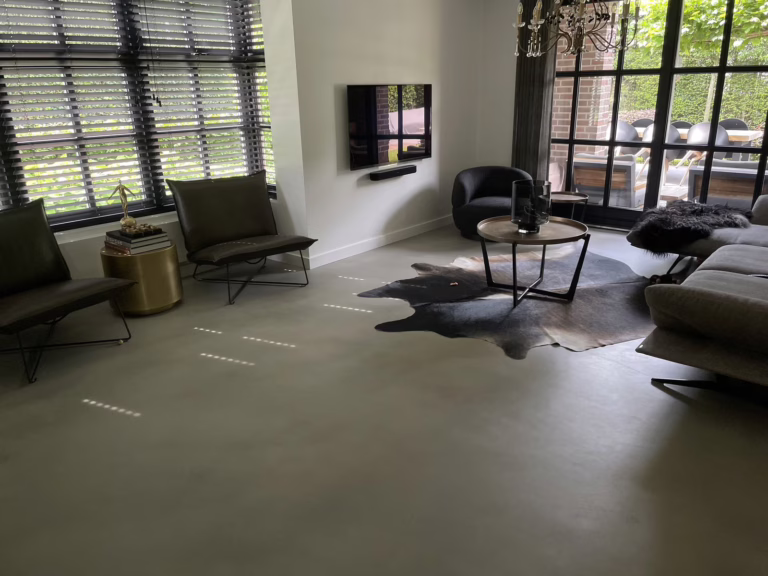 Design Woonbeton in Sint-Michielsgestel, warme grijze microcement vloer in de woonkamer met leren fauteuils en koeienhuid