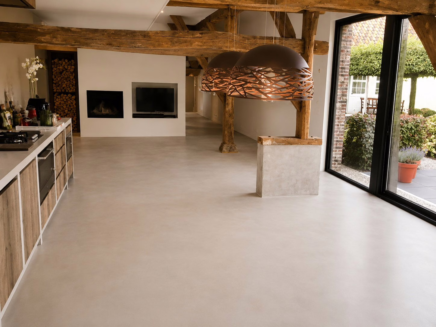 Zithoek met openhaard, houten spanten en pendellampen op een industriele betonnenvloer in Sand Stone, bijgebouw Best