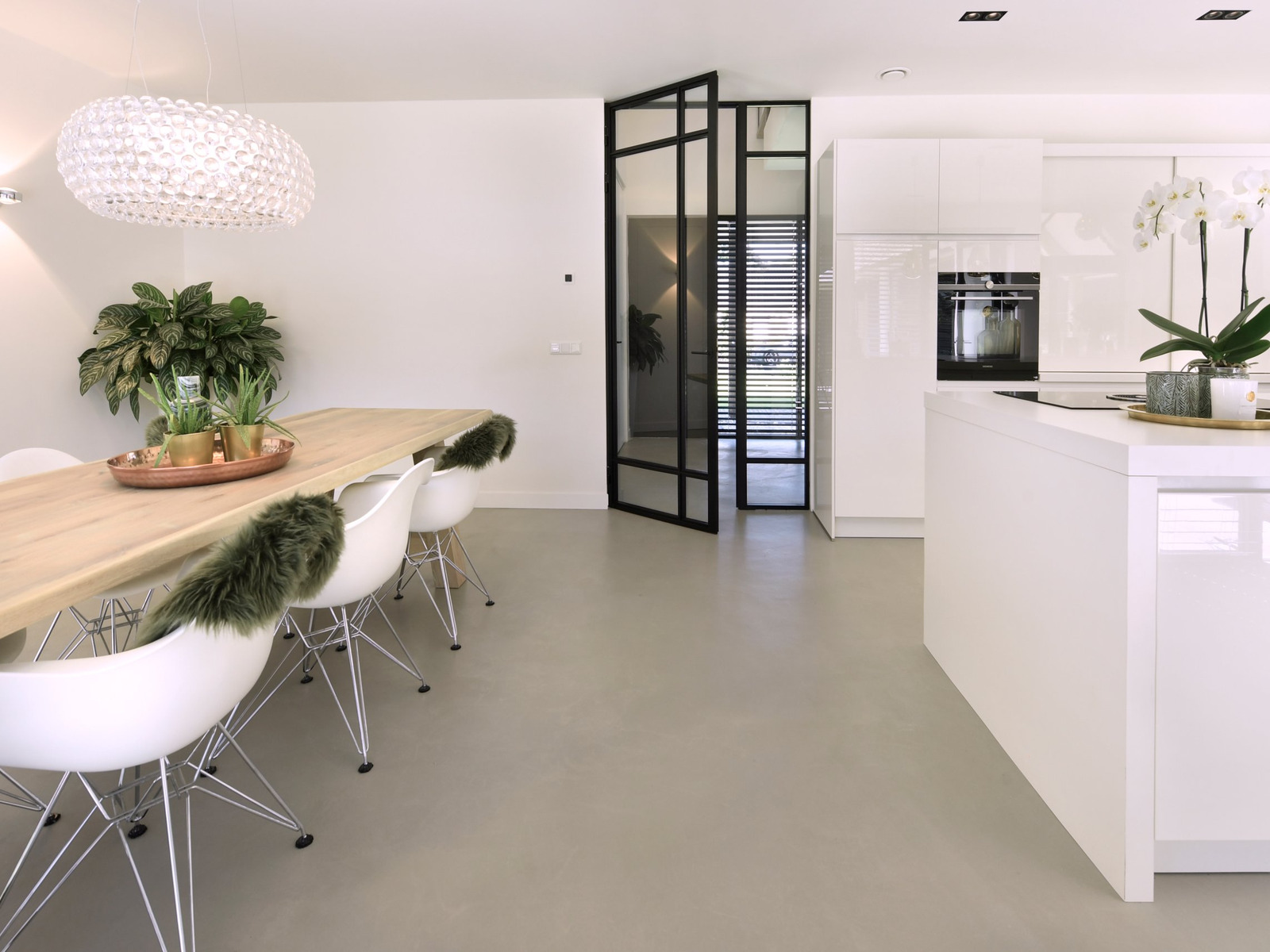 Design Woonbeton in de kleur Stone Grey in een witte eetkeuken met eikenhouten tafel, stalen deur en keukeneiland in Schijf