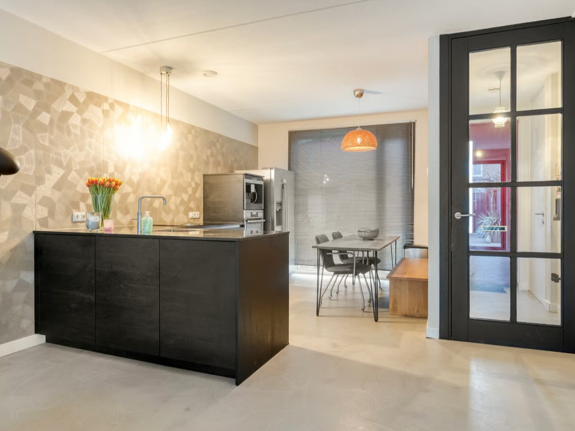 ndustriële betonnen vloer in de kleur Grigio Quarzo in een open keuken met zwart keukenblok, eethoek en glazen binnendeur in Eindhoven