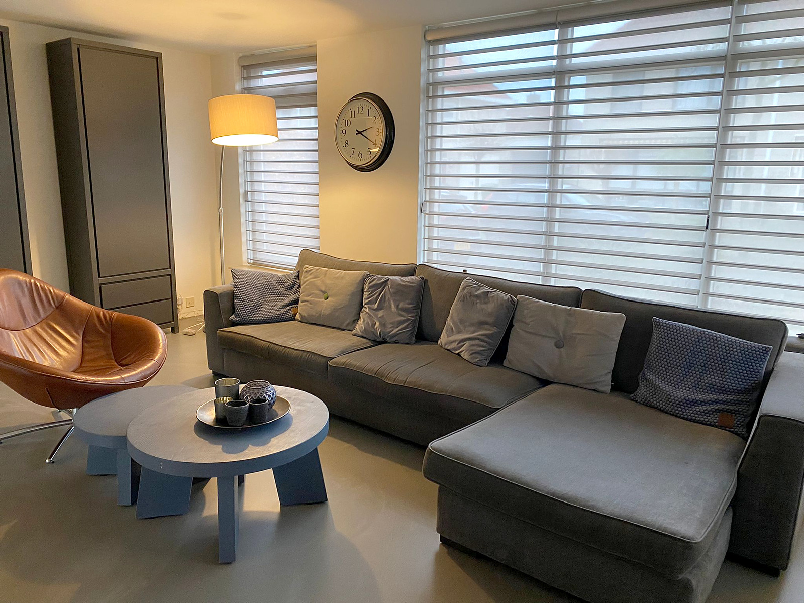 Living Quartz Stone gietvloer Emperador Grey woonkamer Roermond Living Quartz Stone gietvloer in de kleur Emperador Grey in een woonkamer met grijze hoekbank, leren fauteuil en ronde salontafels in Roermond